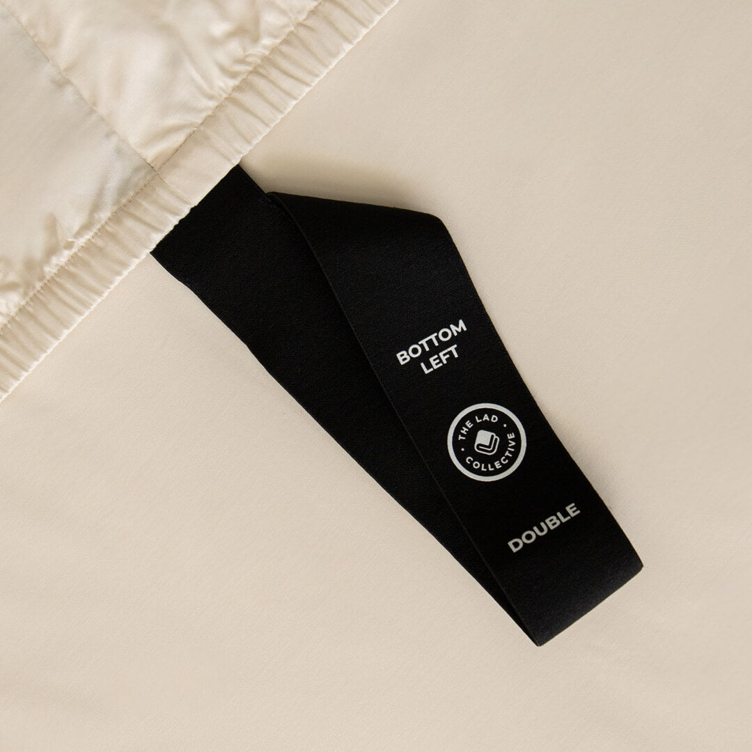 Black labelled corner loop strap that says 'Bottom Left' on cream fitted sheet.