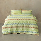 Striped green and brown bedding set on a bed against a beige wall.