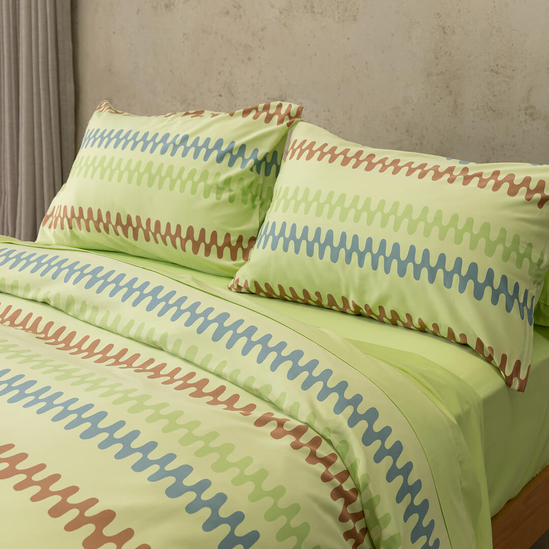 Green bedspread with colorful zigzag pattern on a bed against a neutral wall.