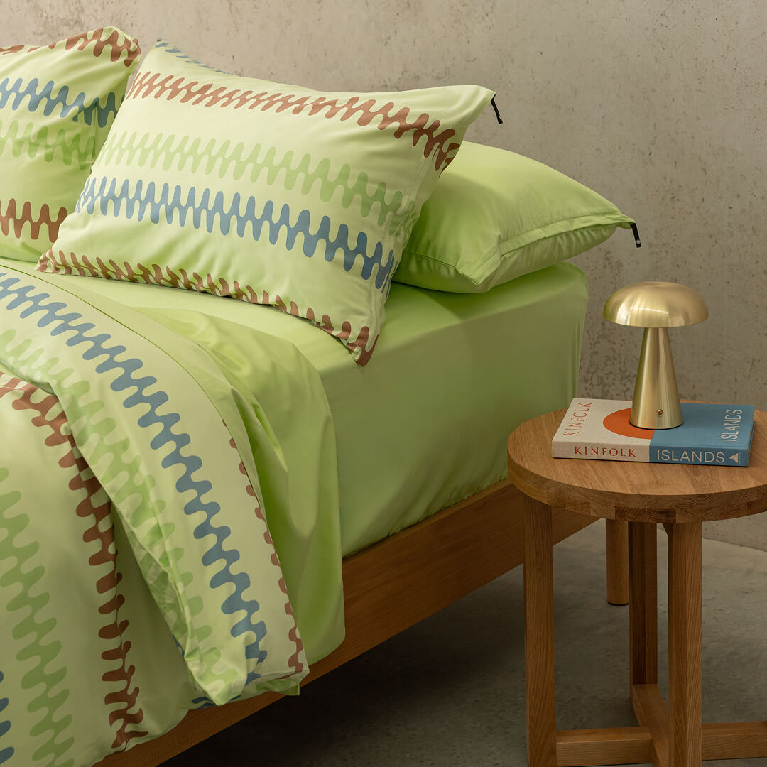 Green bedspread with zigzag pattern on a bed in a room with a side table and lamp.