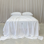 White bedspread with a brand logo on a bed against a neutral background.