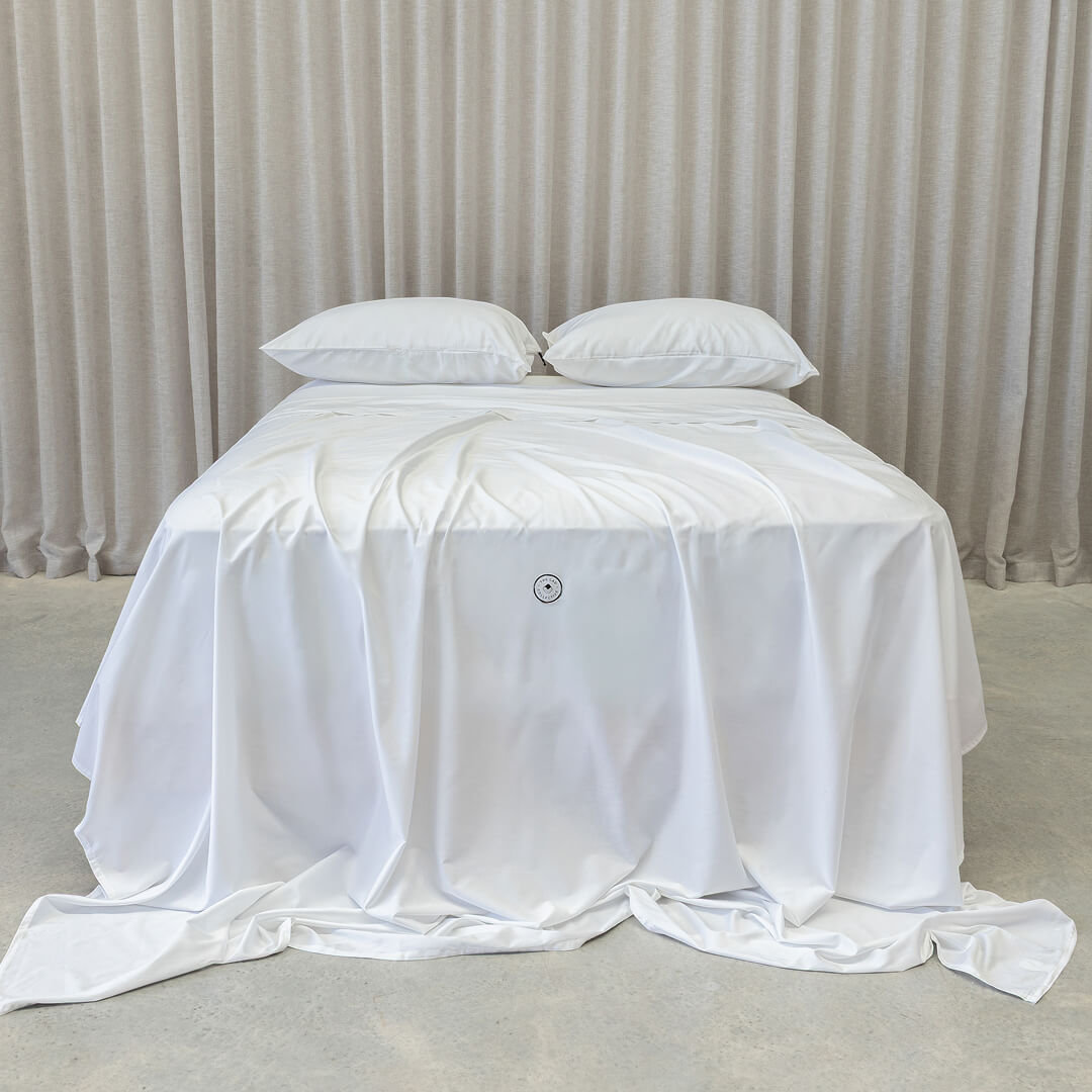 White bedspread with a brand logo on a bed against a neutral background.