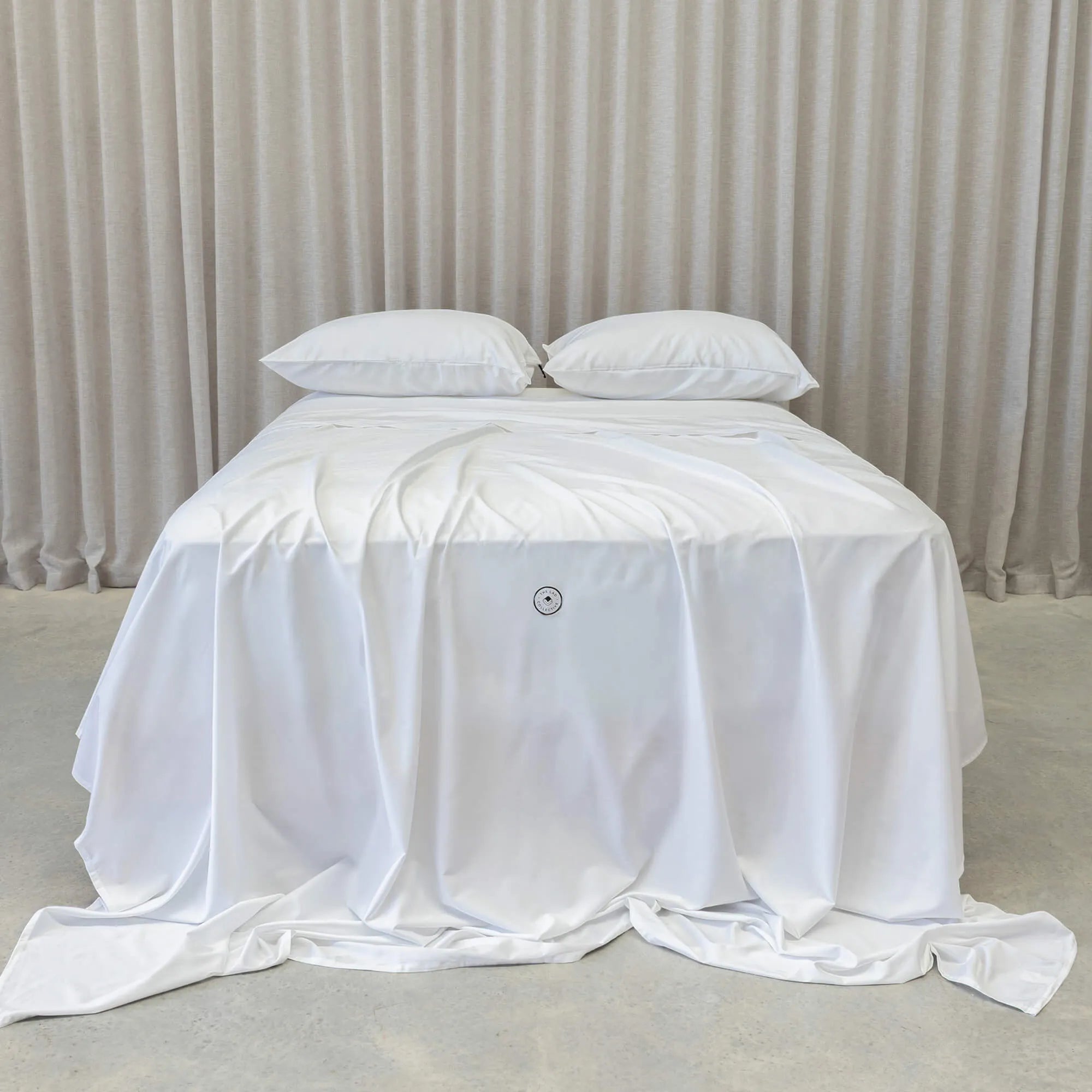 White bedspread on a bed with white pillows against a beige curtain background