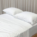 White bedspread and pillows on a bed with beige curtains in the background