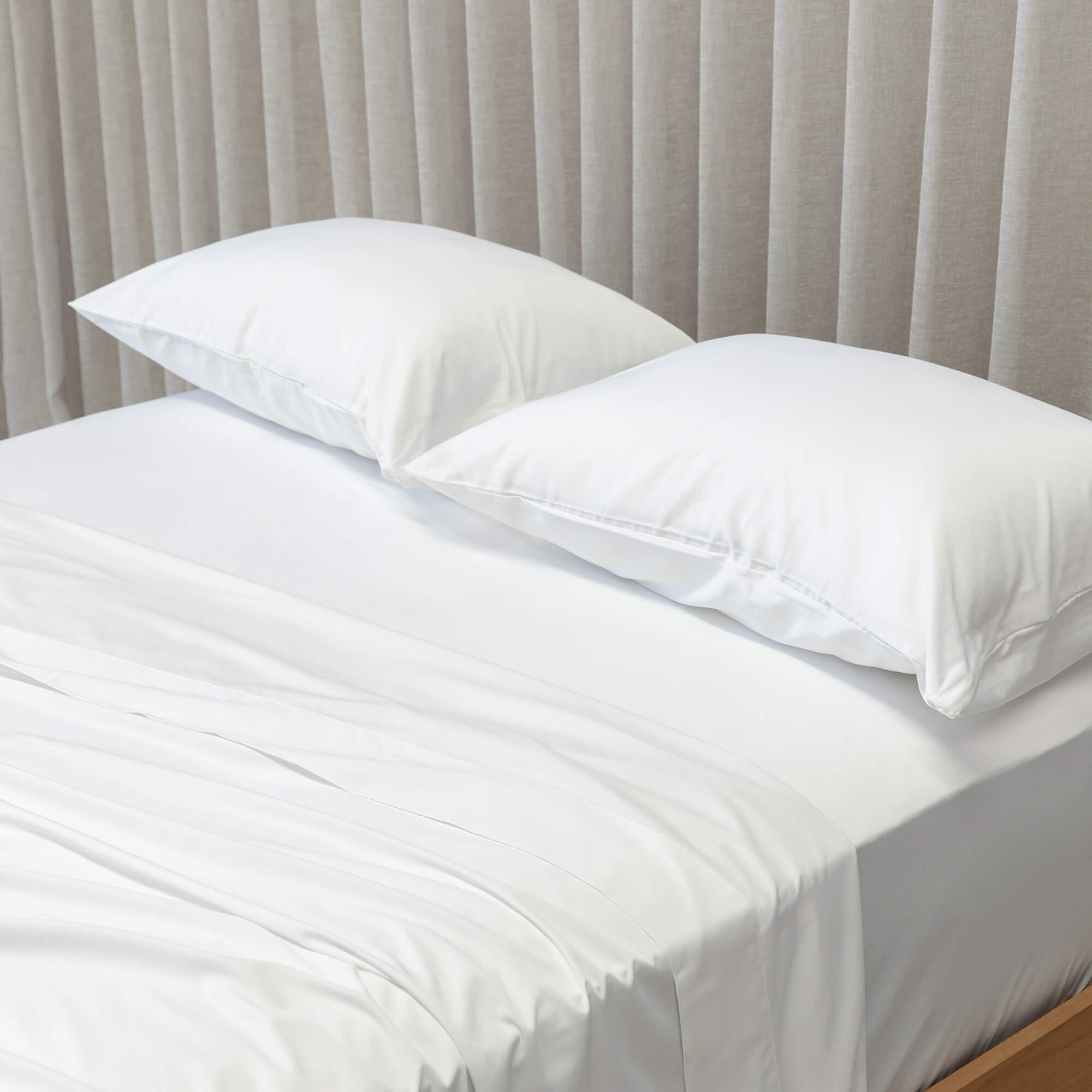 White bedspread and pillows on a bed with beige curtains in the background