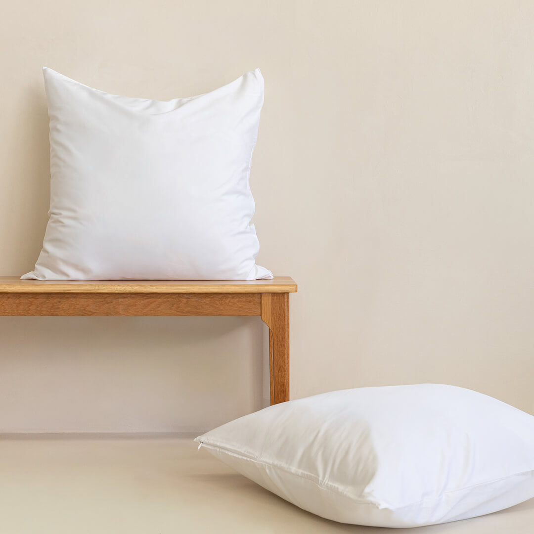 Two white Euorpean pillowcases on a timer bench, with a neutral background.