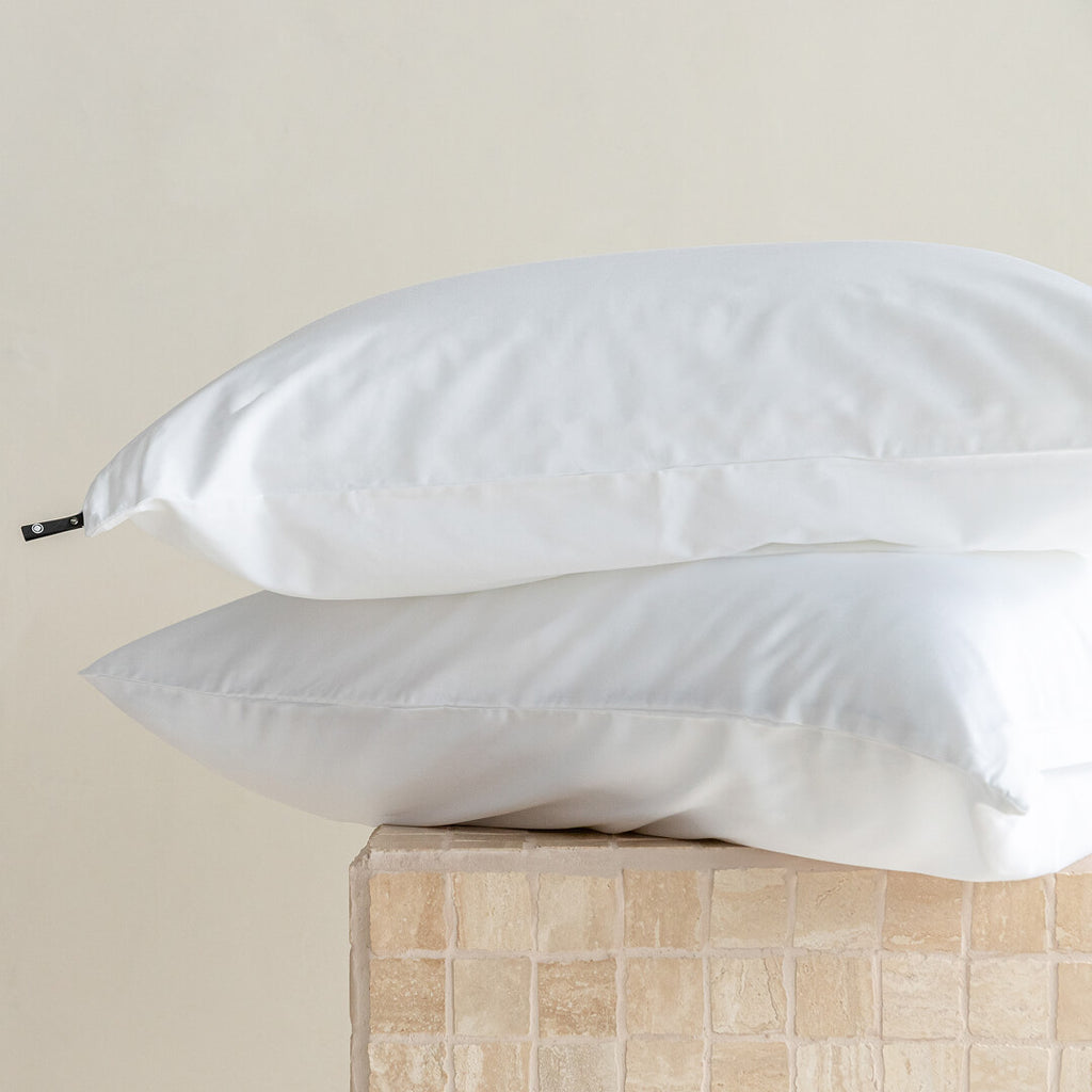 Two white pillows on a beige surface with a neutral background.
