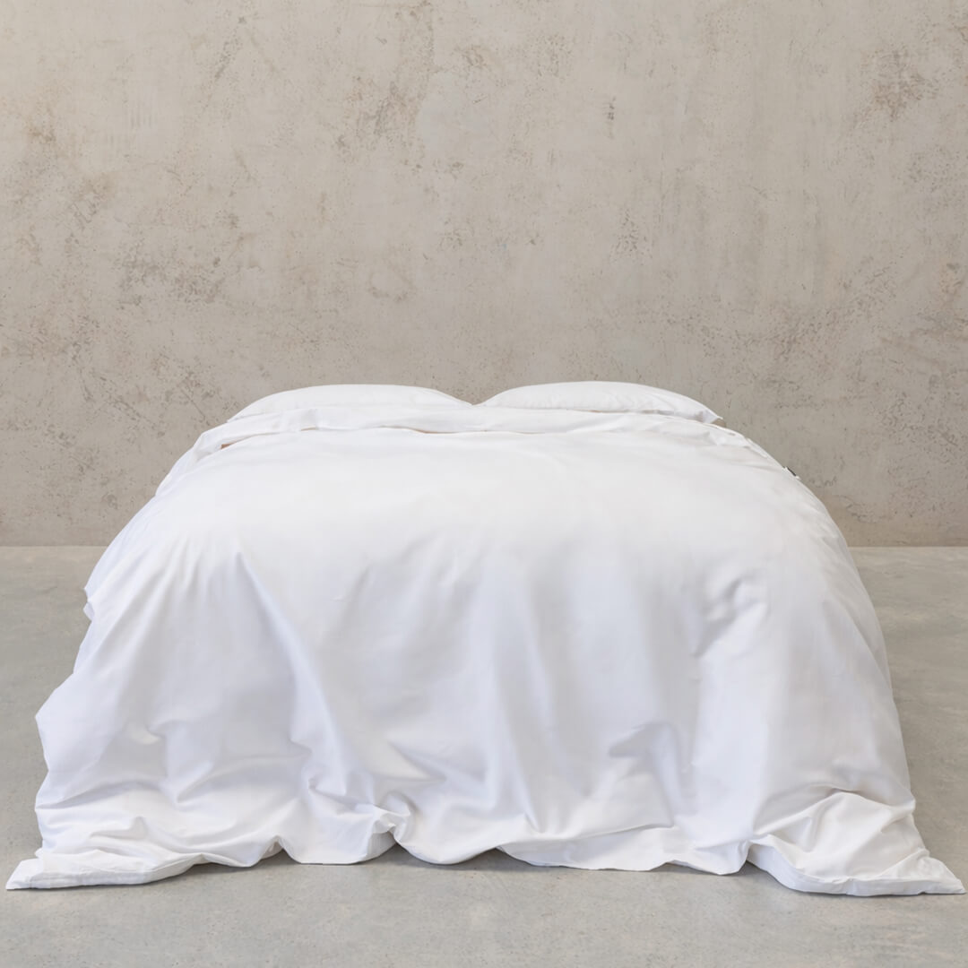 White comforter on a bed against a plain wall.