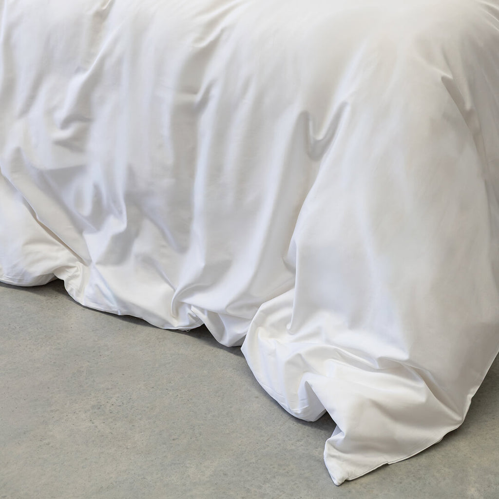 White comforter on a bed with a neutral background.