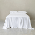 Bright white fitted sheet set styled on a neatly made bed with matching pillowcases, featuring a crisp, clean appearance, soft drape, and minimalist bedroom aesthetic.
