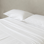Close-up of bright white fitted sheets and matching pillowcases, highlighting the smooth brushed texture, fresh appearance, and comfortable finish.