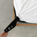 Bright white fitted sheet with an extended orientation tag at the mattress corner, demonstrating the easy-to-locate labeling system for faster bed setup.