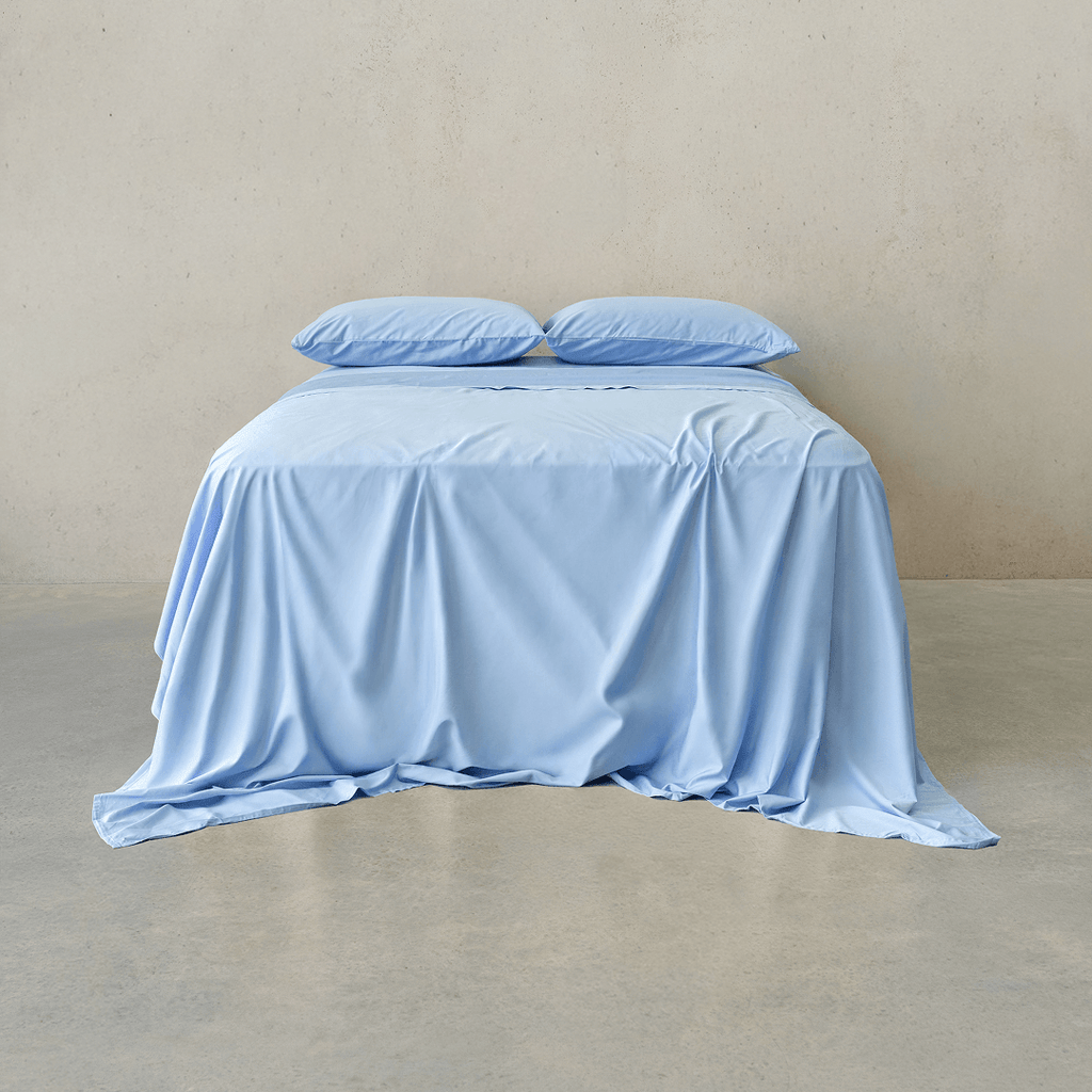 Sky blue bed sheet set draped over a double bed with two matching pillowcases against a neutral wall