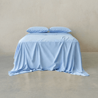 Sky blue bed sheet set draped over a double bed with two matching pillowcases against a neutral wall