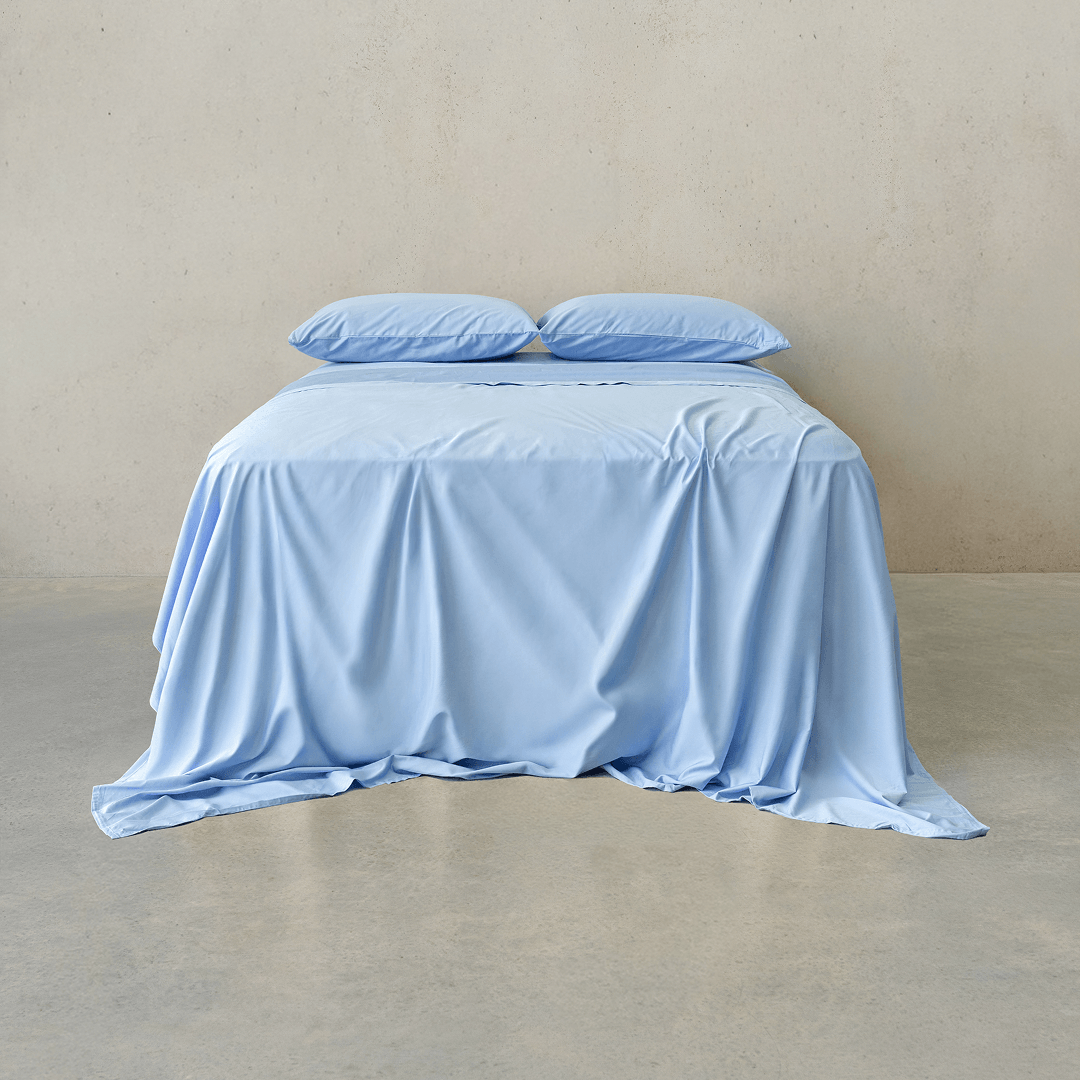 Sky blue bed sheet set draped over a double bed with two matching pillowcases against a neutral wall