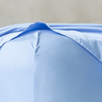 Close-up corner detail of a sky blue fitted sheet and top flat sheet showing smooth fabric texture and seam stitching