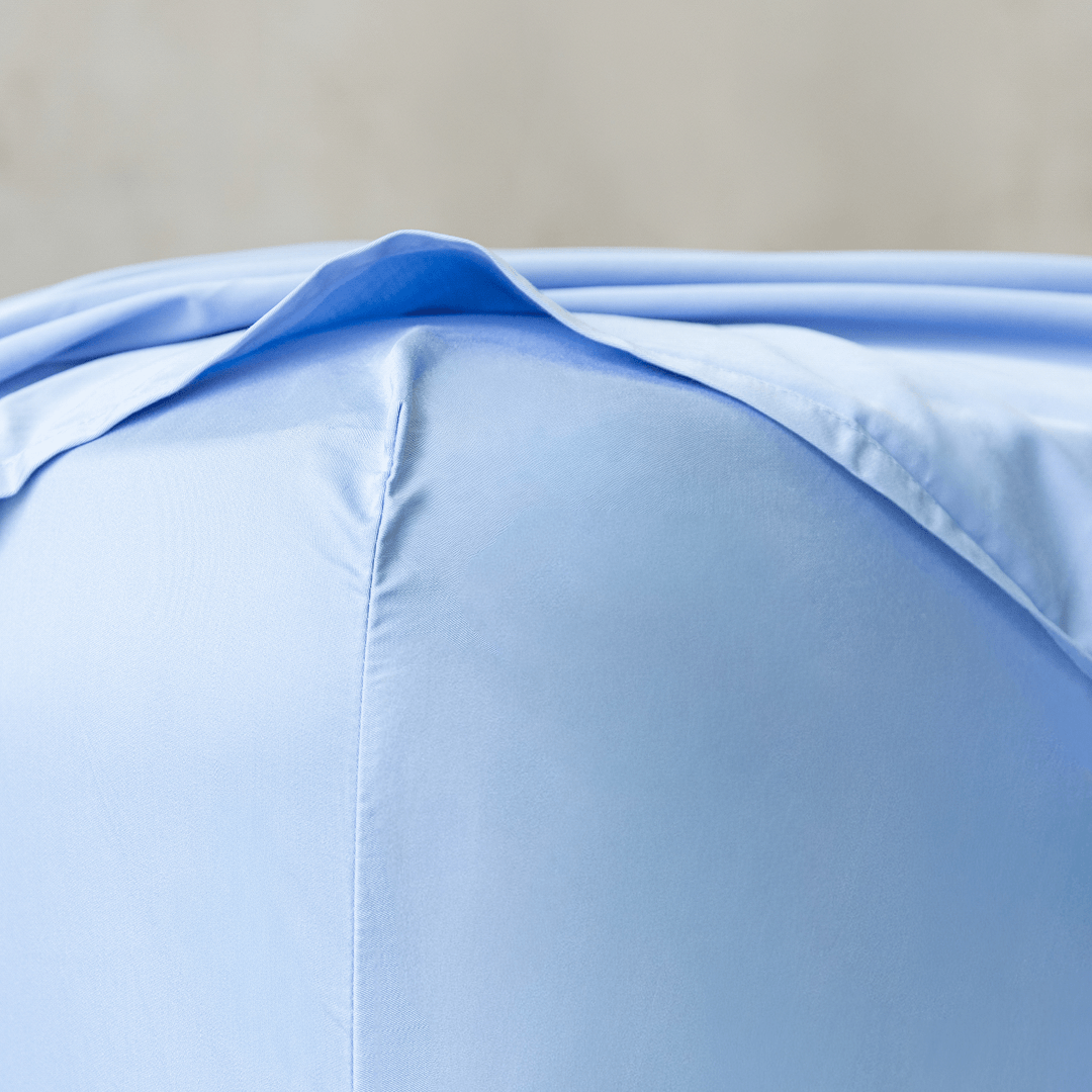 Close-up corner detail of a sky blue fitted sheet and top flat sheet showing smooth fabric texture and seam stitching