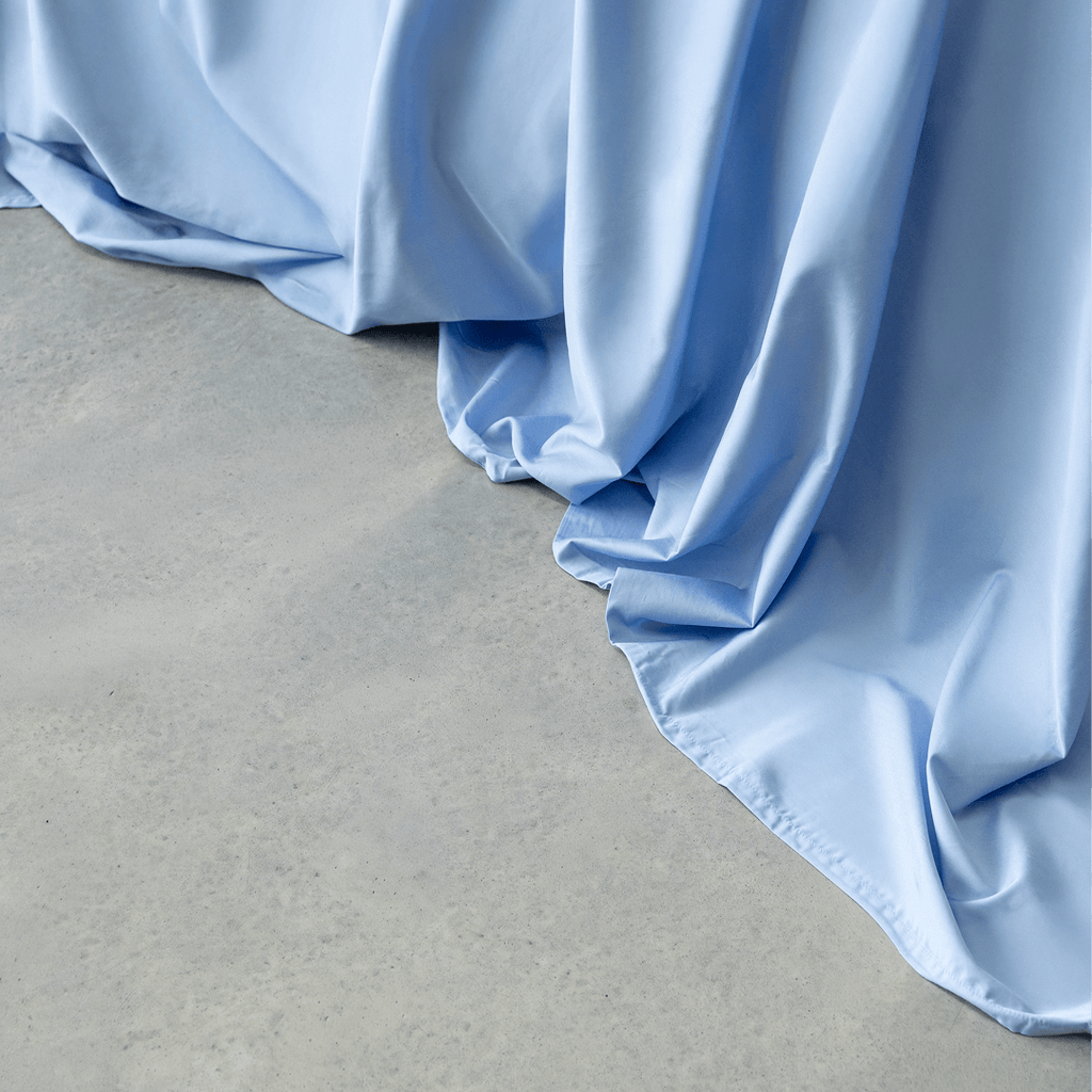 Close-up of sky blue sheet fabric cascading smoothly onto a light gray concrete floor