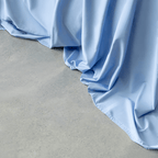 Close-up of sky blue sheet fabric cascading smoothly onto a light gray concrete floor