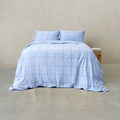 Light blue grid-patterned quilt cover set made up on a double bed with two matching pillowcases against a neutral wall