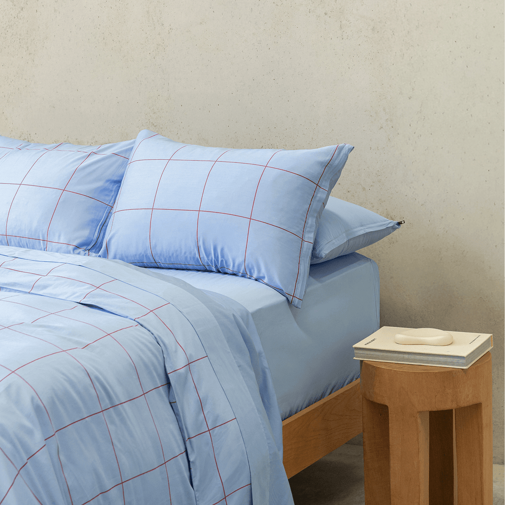 Side view of a double bed styled with a light blue grid-patterned quilt cover and matching pillowcases next to a wooden nightstand