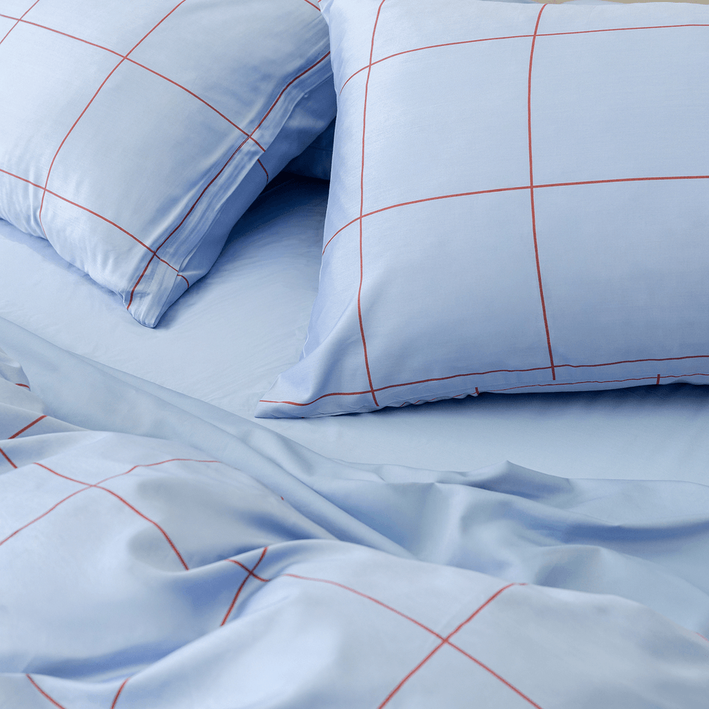 lose-up of two light blue grid pillowcases resting on a matching solid light blue sheet and rumpled quilt cover