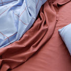Close-up view of light blue grid quilt cover draped over rumpled rust red flat sheet