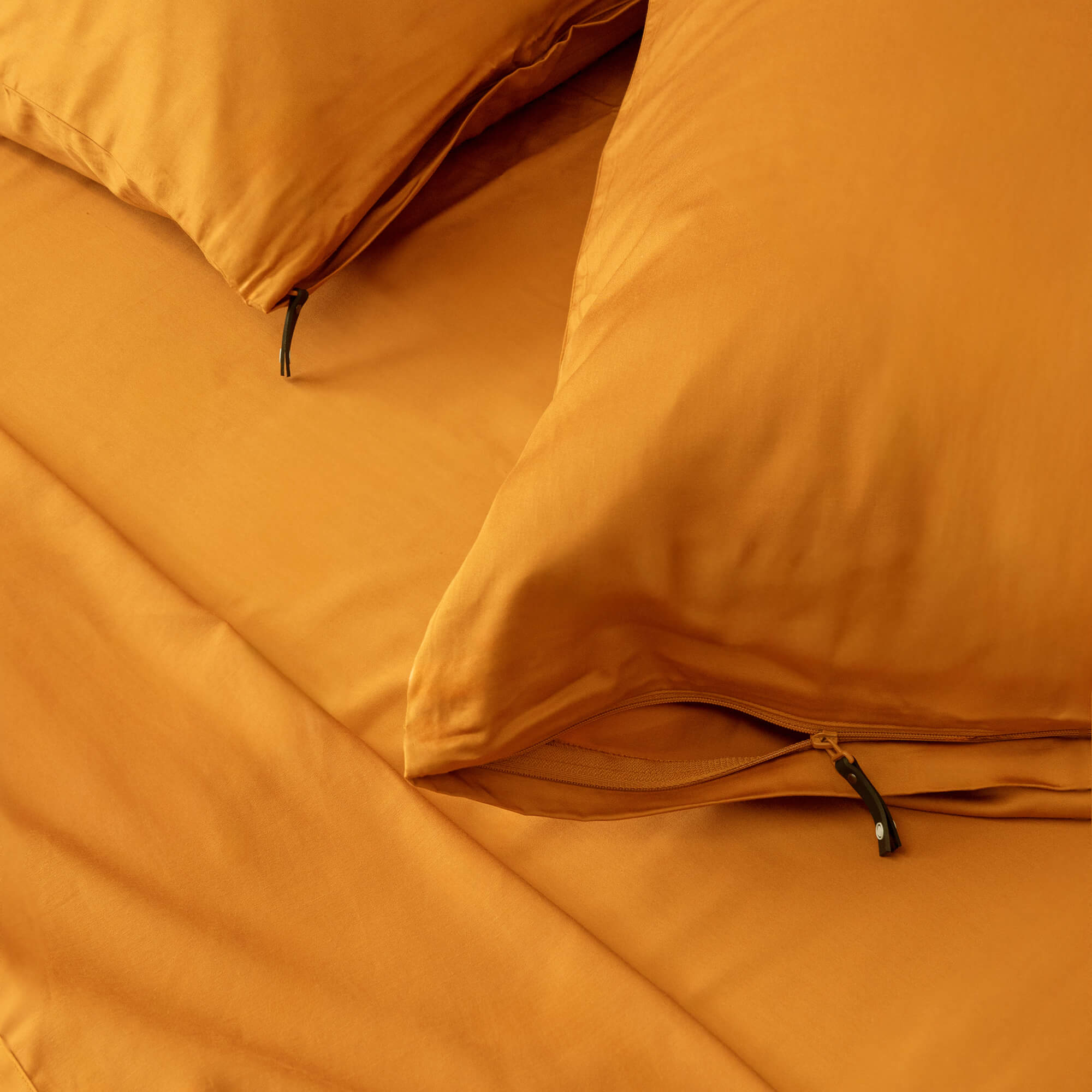 Close up of orange pillowcases with zipper detail on orange bedspread