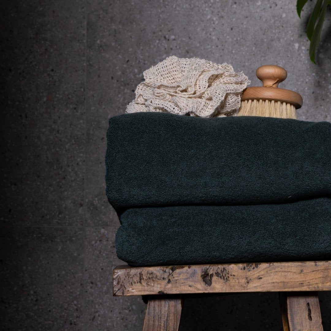 Stack of dark green towels with a wooden brush and white lace on a grey background.