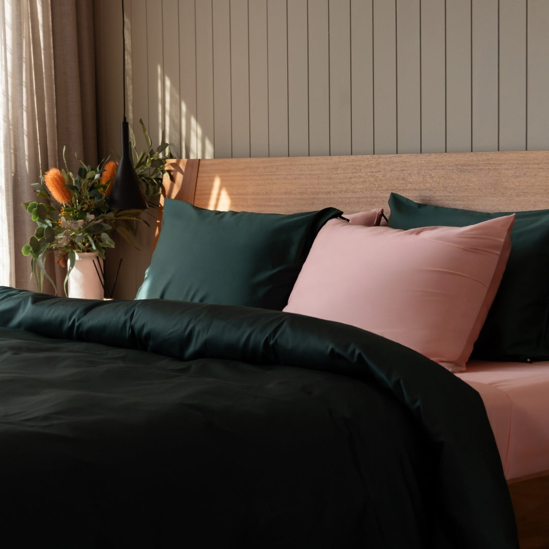 Bed with dark green and pink pillows against a wooden headboard.