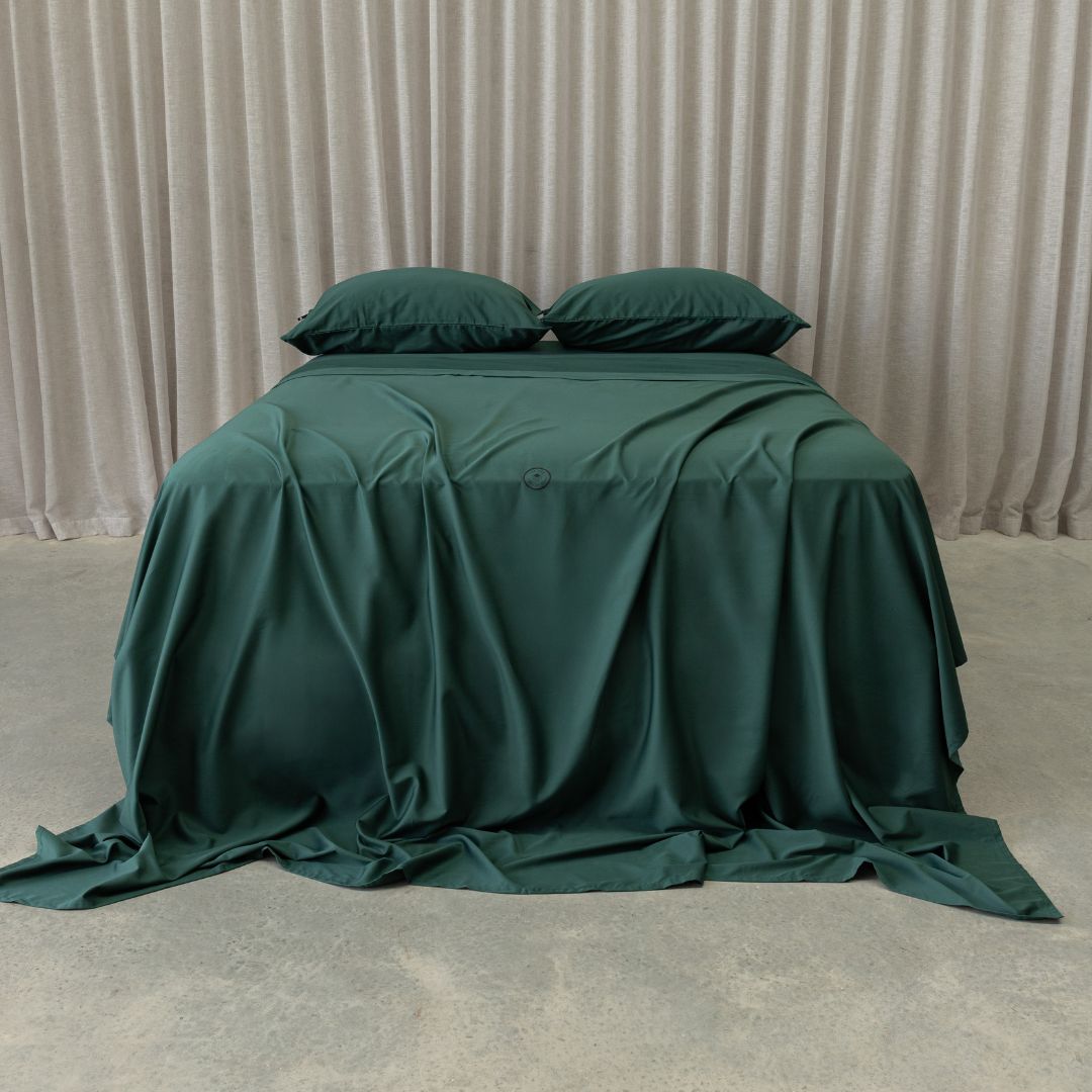 Green bedspread and pillows on a bed with beige curtains in the background