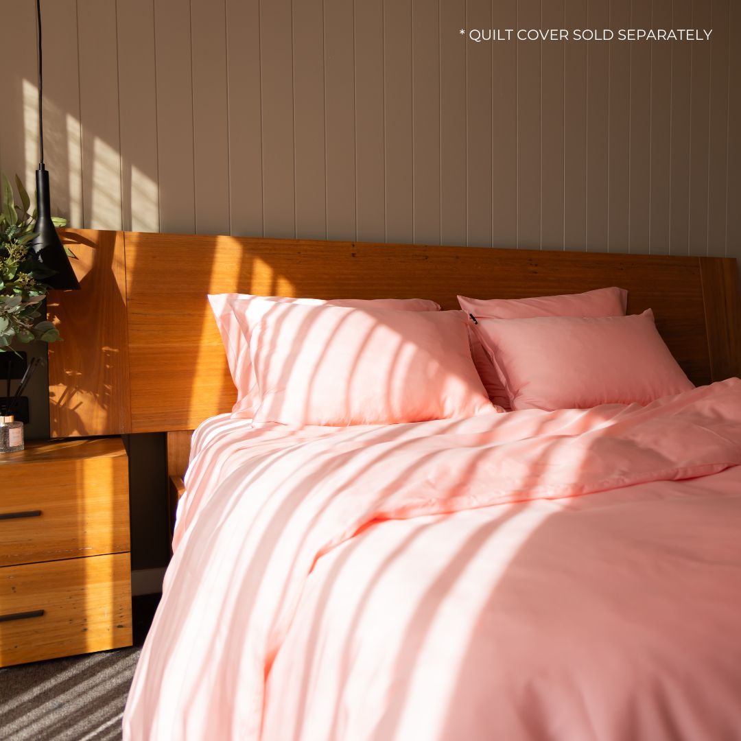 Bed with pink bedding and pillows in a bedroom setting. 