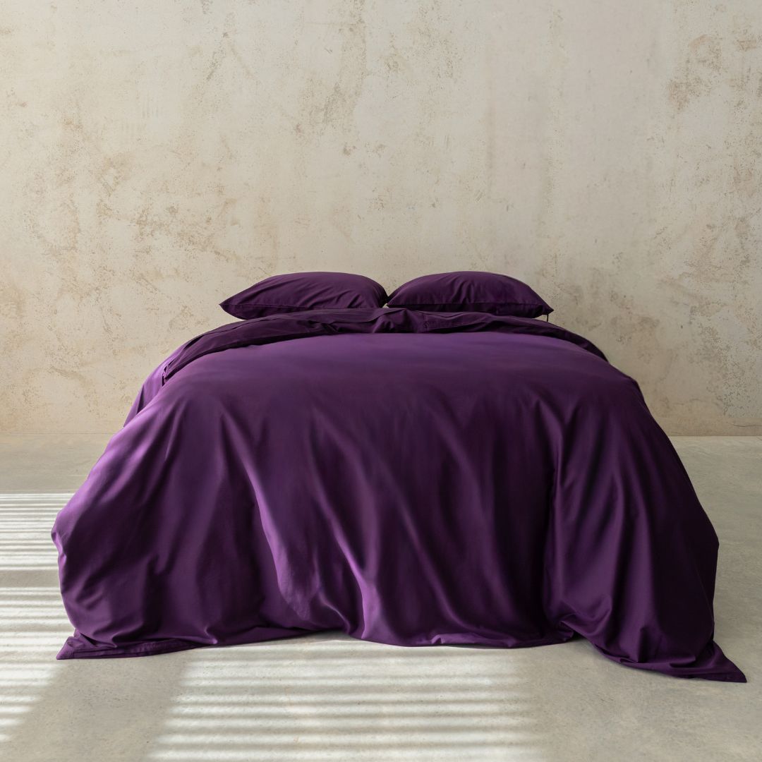 Purple bedding set on a bed against a beige wall.