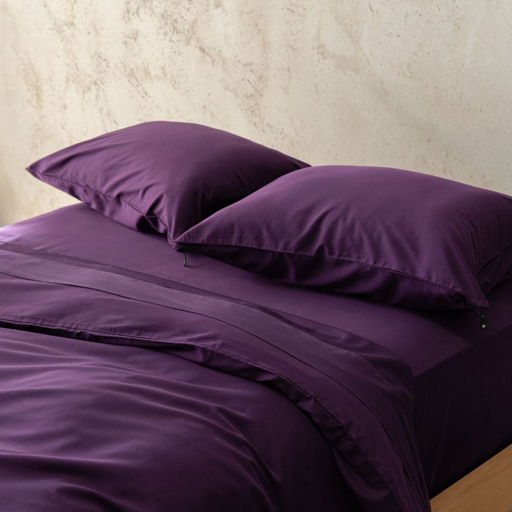 Purple bedding set with two pillows on a bed against a neutral wall.
