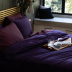 Bedroom with purple bedding and pillows, a tray with items on a windowsill.