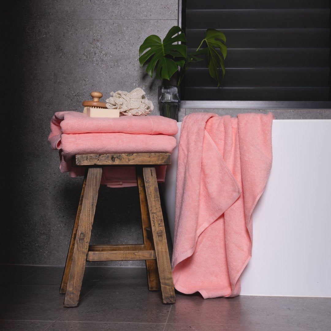 Pink towels draped over a wooden stool against a dark wall with a plant in the background.