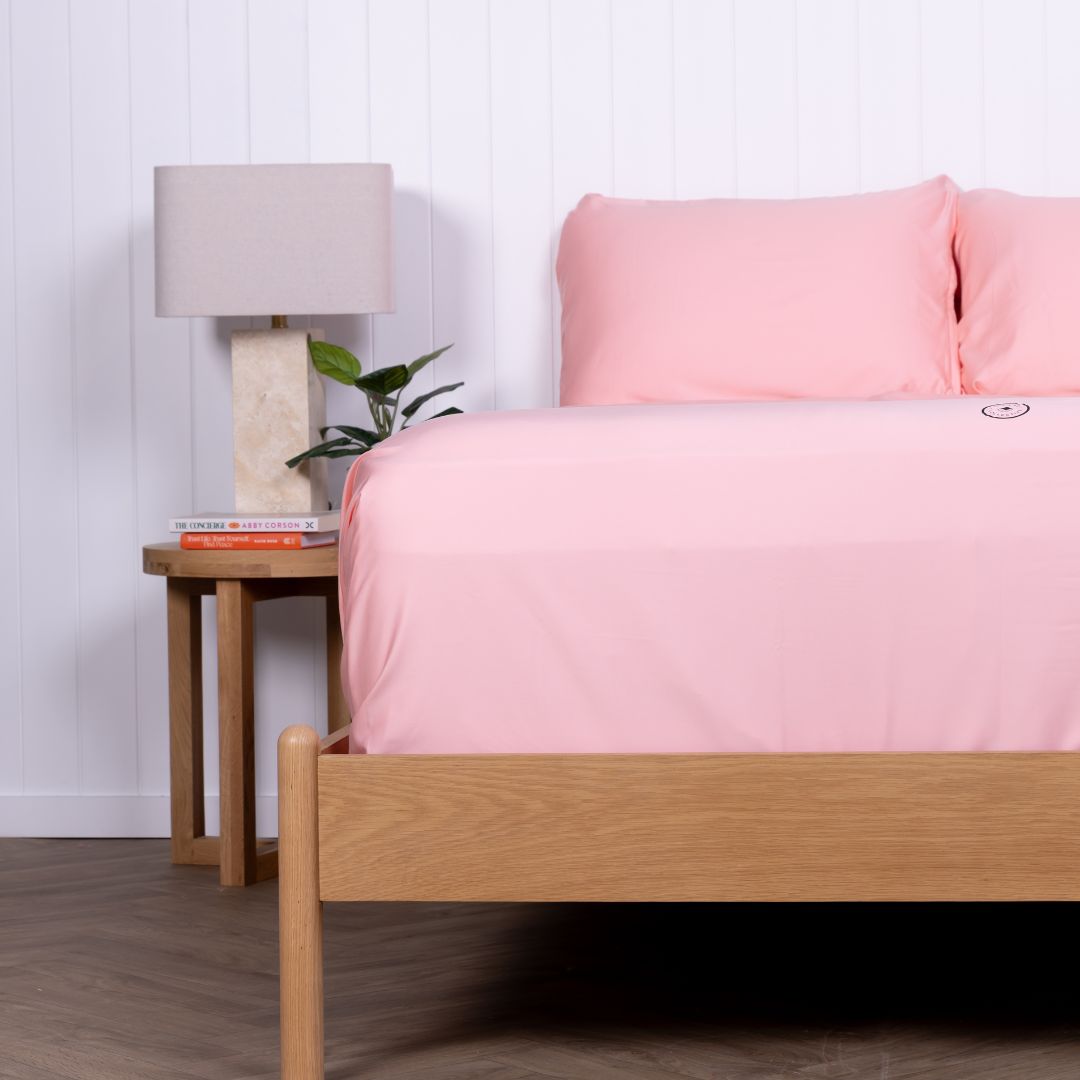 Side angle of pink Streak Bay bedding on bed next to wooden bedside table.
