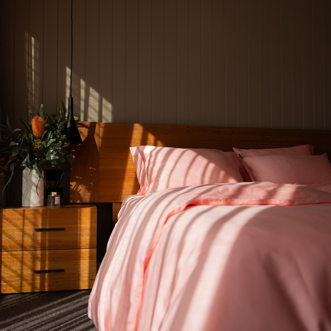 Bedroom with pink bedding and wooden nightstand, sun casting shadows.