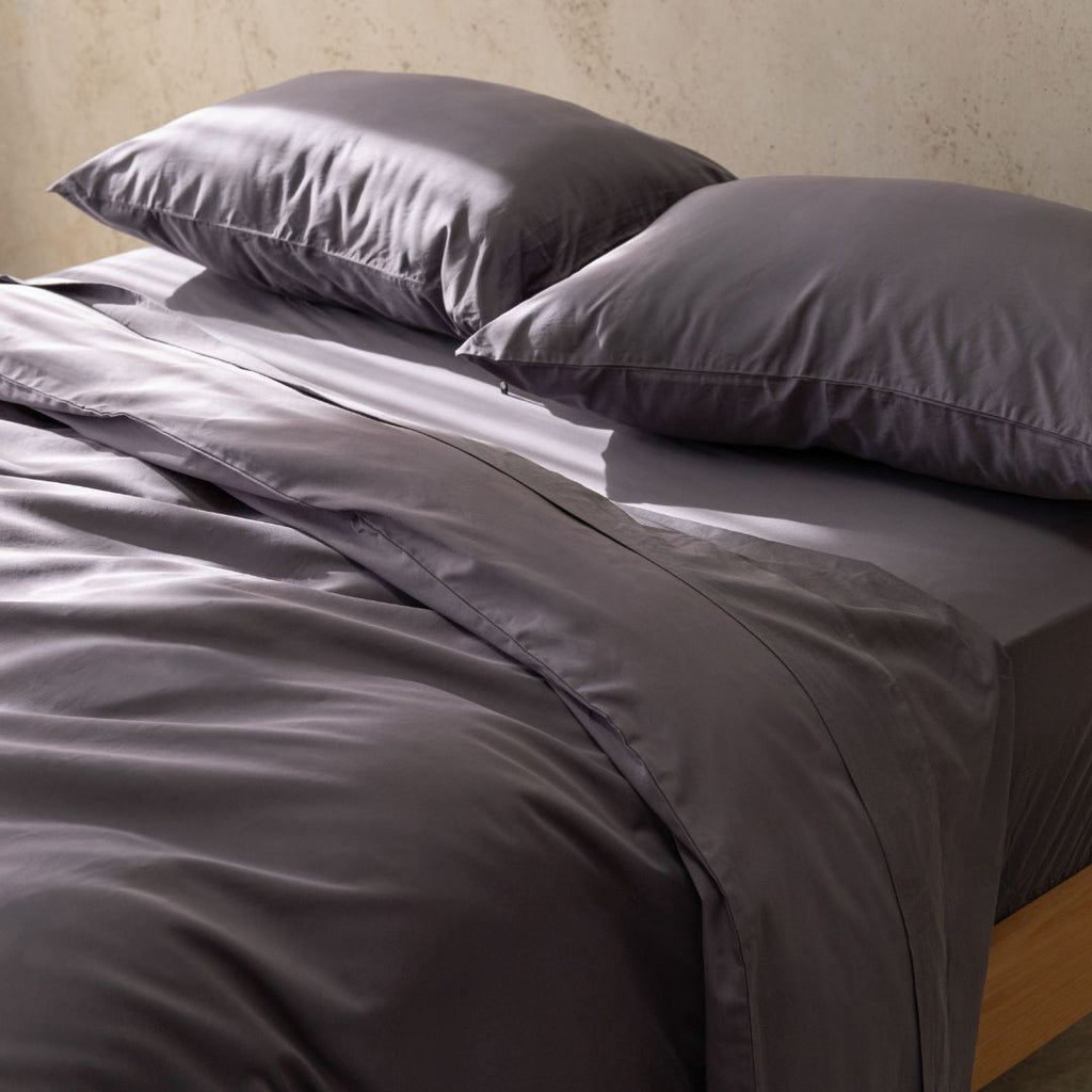 Gray bedding set with two pillows on a bed against a neutral wall.