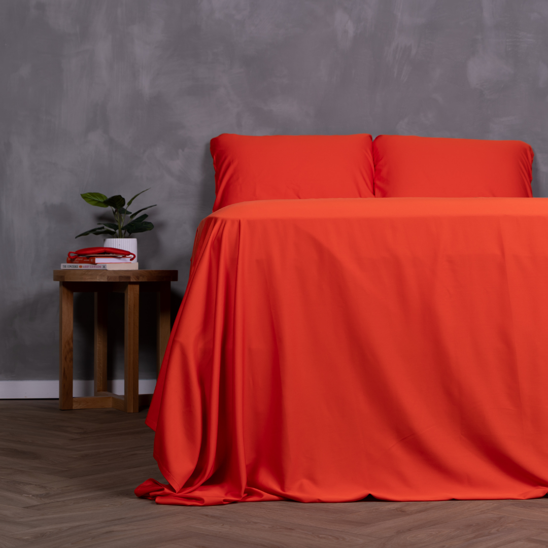 Vibrant red bamboo and cotton bed sheet set styled on a queen bed with matching pillows and bedside table.