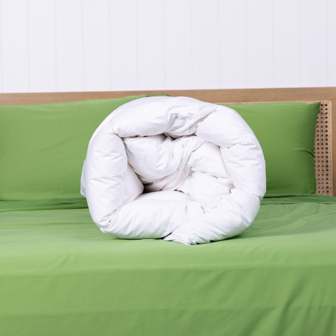 Rolled white comforter on a green bed with a white wall background