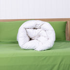 Rolled white comforter on a green bed with a white wall background