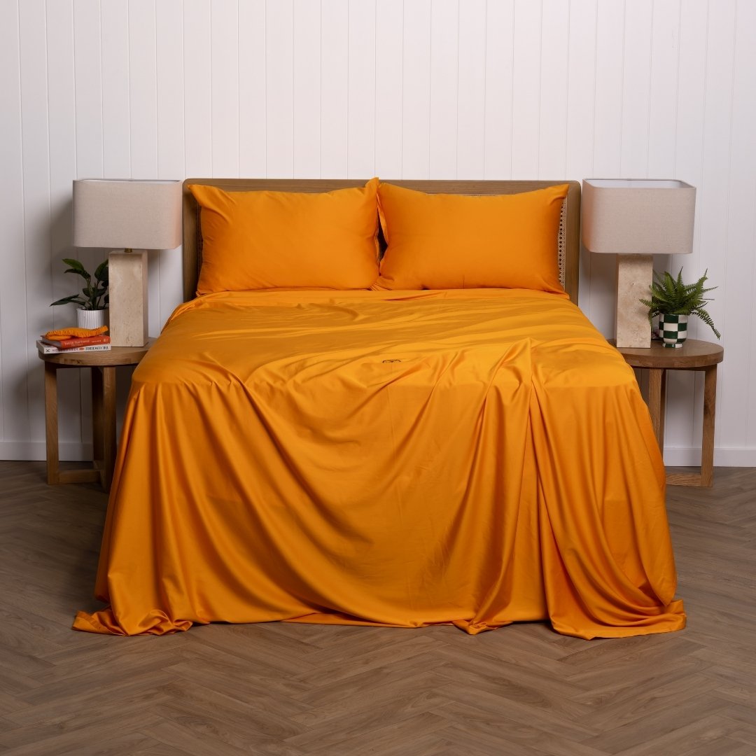 Orange bedspread and pillows on a bed with side tables and lamps in a room.