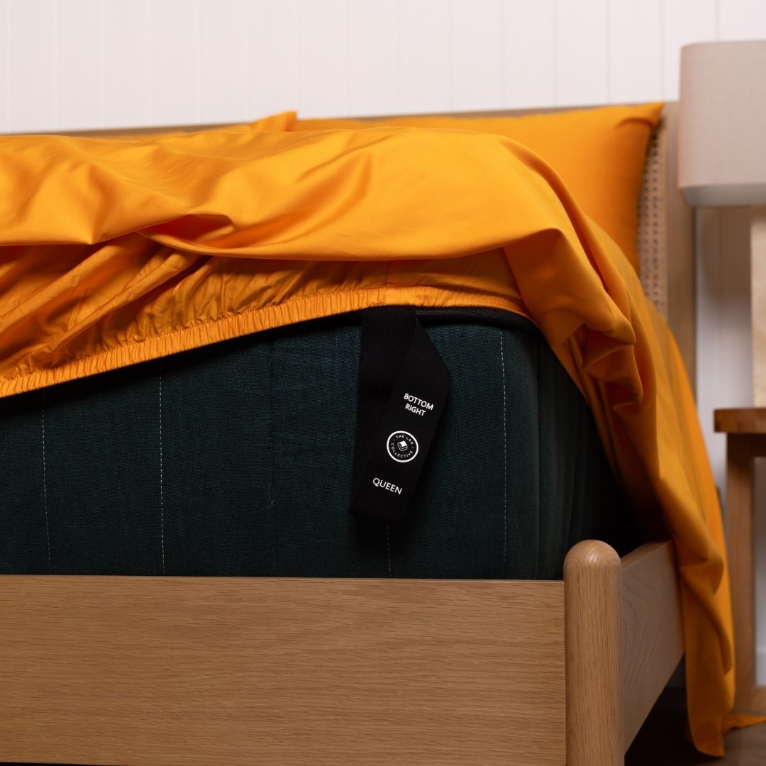 Bed with orange bedding and a labelled corner loop strap on a mattress/wooden bed frame.