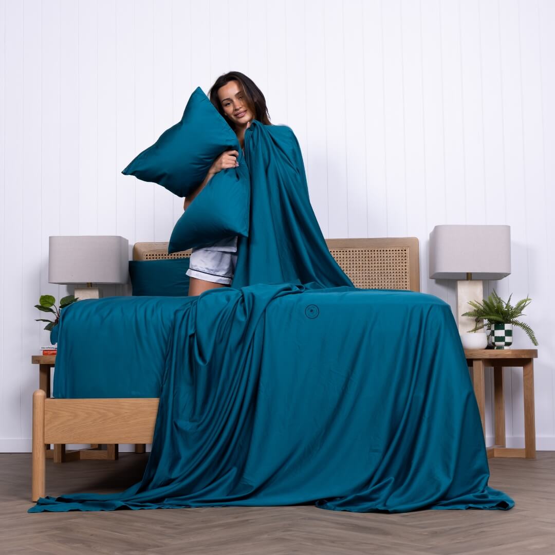 Woman wrapped in rich teal bedding from The Lad Collective, showcasing the bold and calming colour of the bamboo-cotton sheet set. 