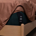 Elastic corner strap labelled ‘Bottom Right’ and ‘Double’ on a dark green mattress under rust-coloured sheets.