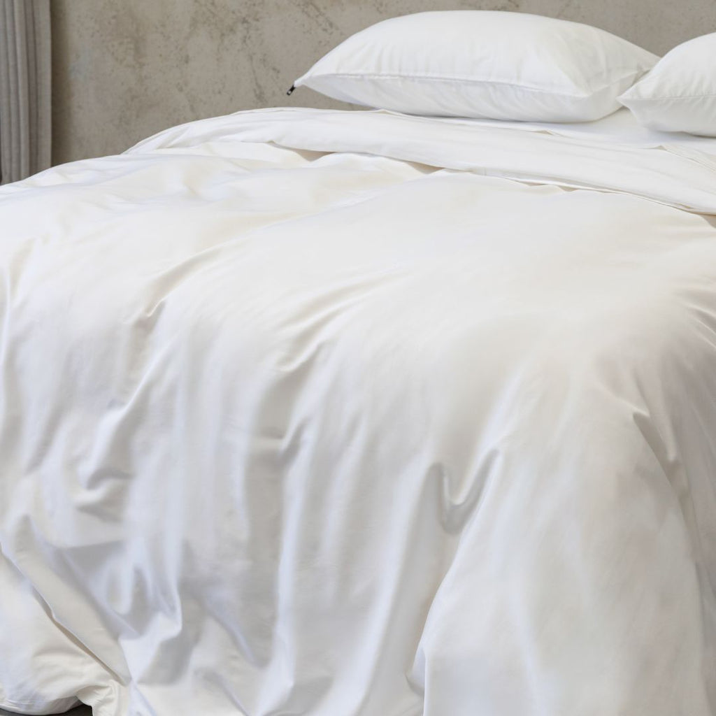 White quilt on a bed with pillows against a neutral wall.