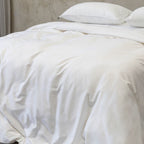 White quilt on a bed with pillows against a neutral wall.