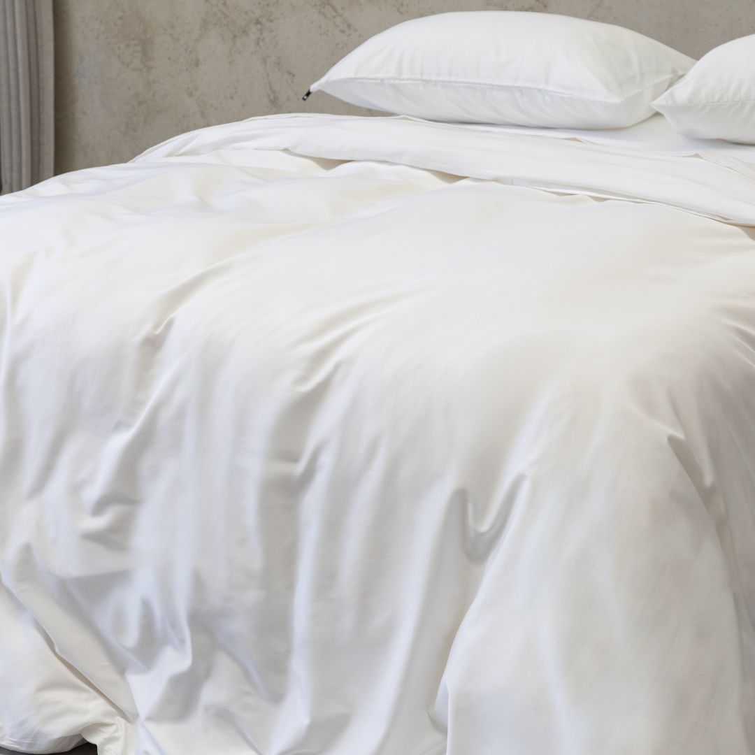 White quilt on a bed with pillows against a neutral wall.