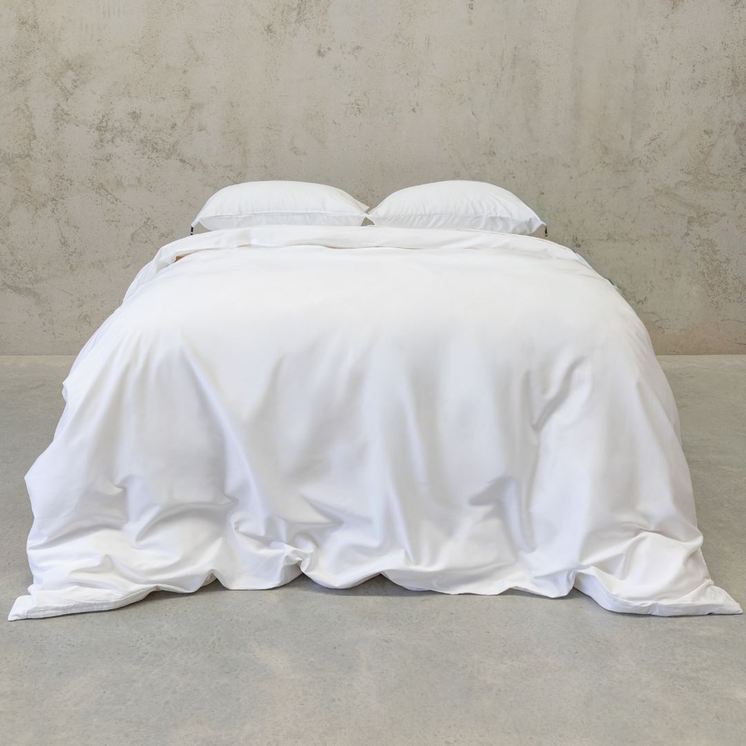 White bedding on a bed with pillows against a neutral wall.